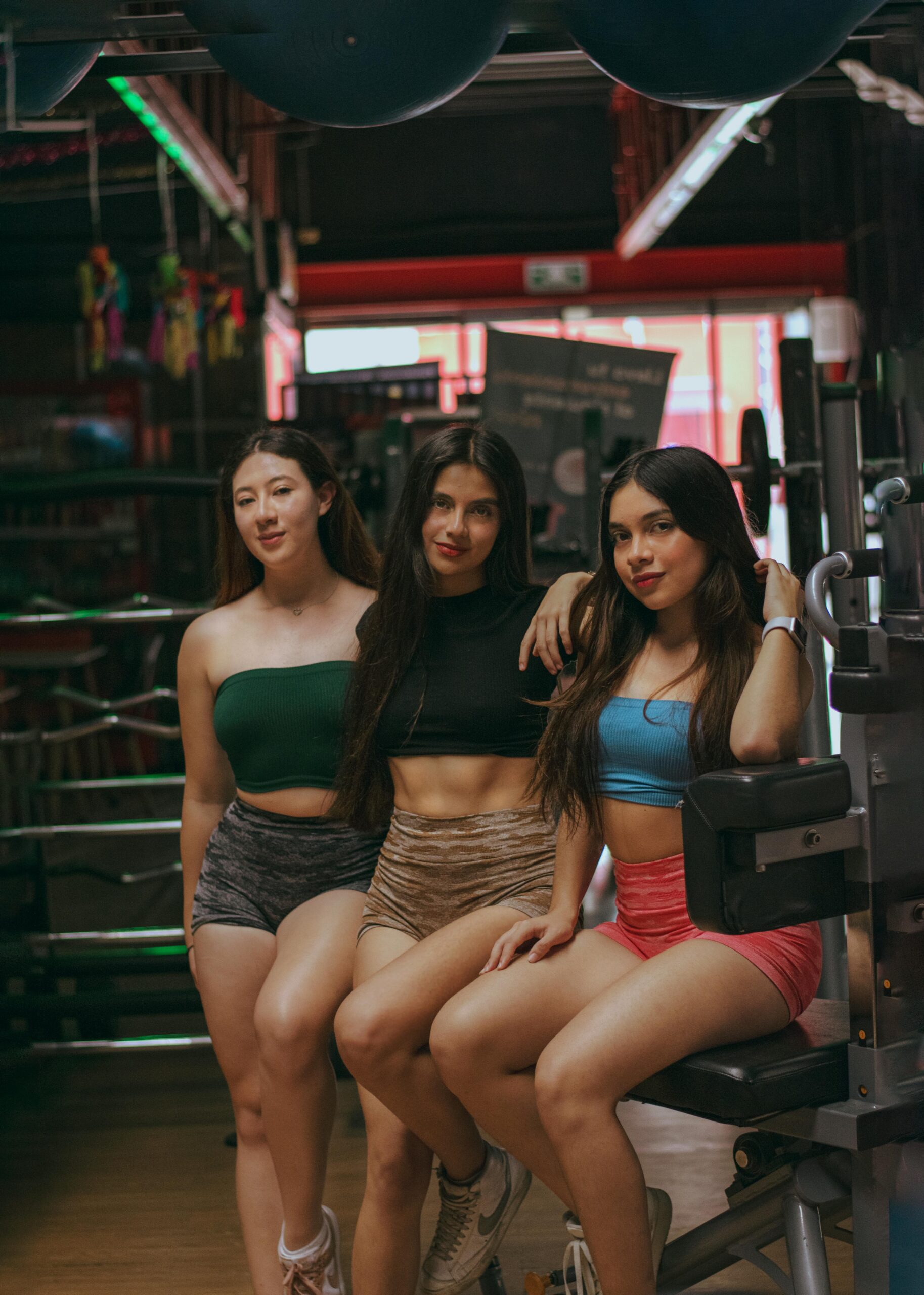 Three confident women posing in a gym, showcasing fitness and friendship.